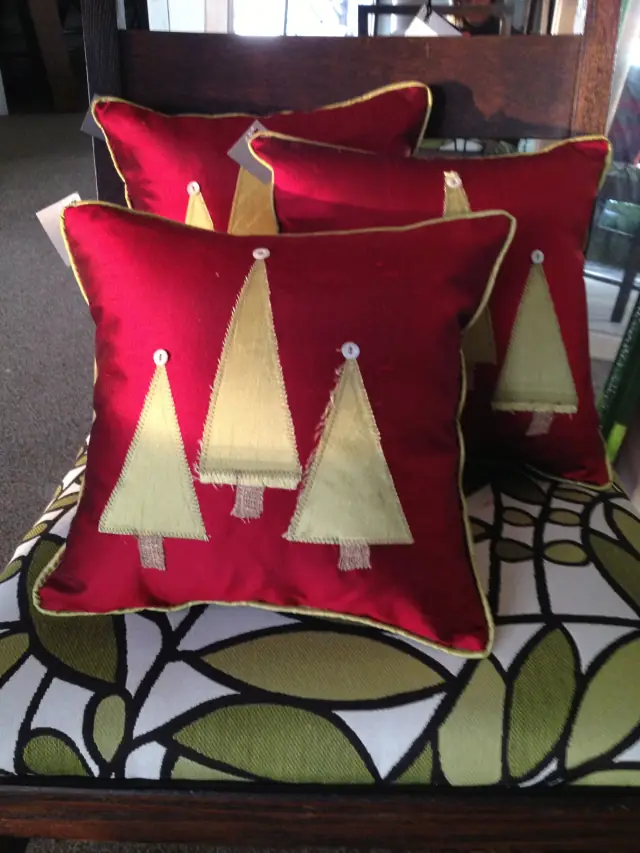 Red pillows with appliqued gold trees on a leaf-print bench
