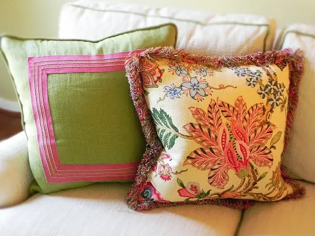 Green linen pillow with a pink border beside a fringed floral pillow